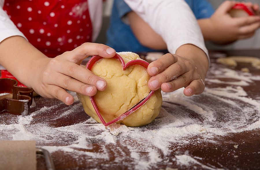Backgruppe Kind formt aus einem Mürbeteig ein Herz mithilfe eines Förmchens