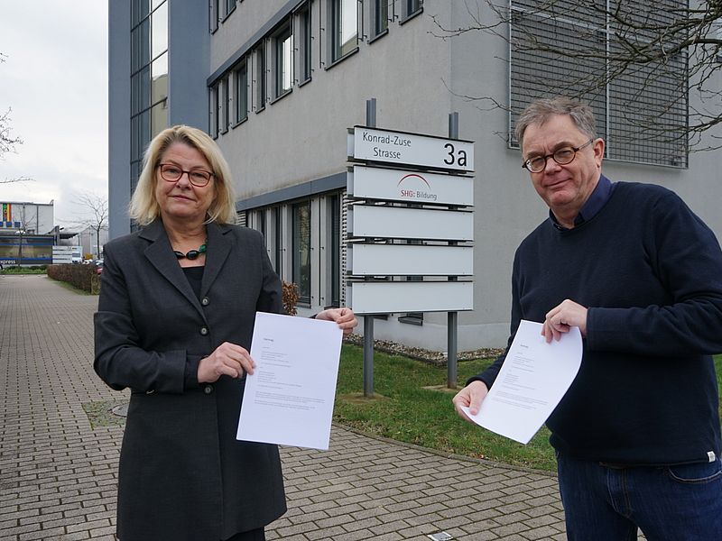 Zwei Personen vor der SHG Bildung präsentieren Dokumente