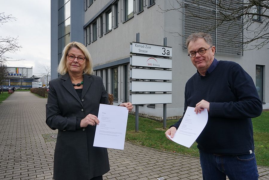 Zwei Personen vor der SHG Bildung präsentieren Dokumente