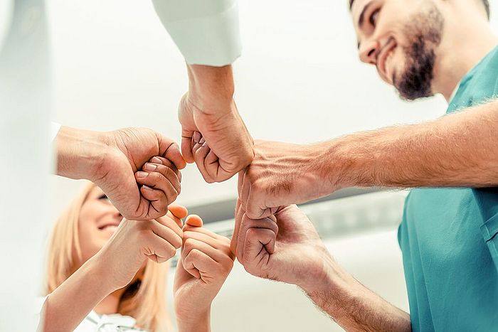 Mehrere Personen in einem Kreis halten ihre Fäuste zusammen