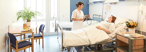 Pflegekraft spricht mit Person in Krankenbett