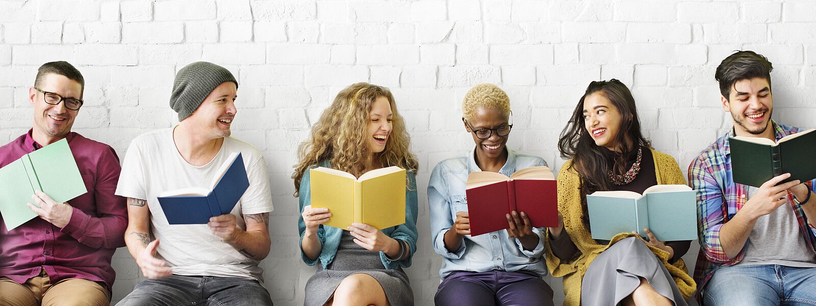 Mehrere Personen mit Büchern in den Händen sitzen an Wand slider_bildung.jpg