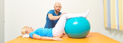 Mann leitet Frau zu Übungen mit Gymnastikball an