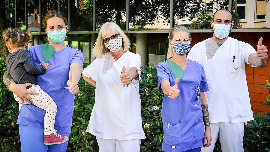 Das Team der Intensivpflege steht mit Masken nebeneinander und zeigt den Daumen nach oben