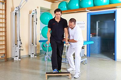 Physiotherapeut trainiert mit einem Patienten das Gehen