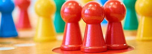 Drei rote Spielfiguren stehen auf einem Spielbrett nebeneinander