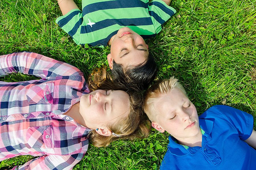 Entspannungsgruppe Drei Kinder liegen mit geschlossenen Augen auf einem Rasen.